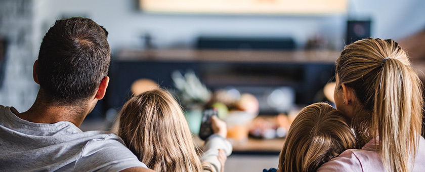 Eine Familie sitzt auf der Couch und schaut zum Fernseher