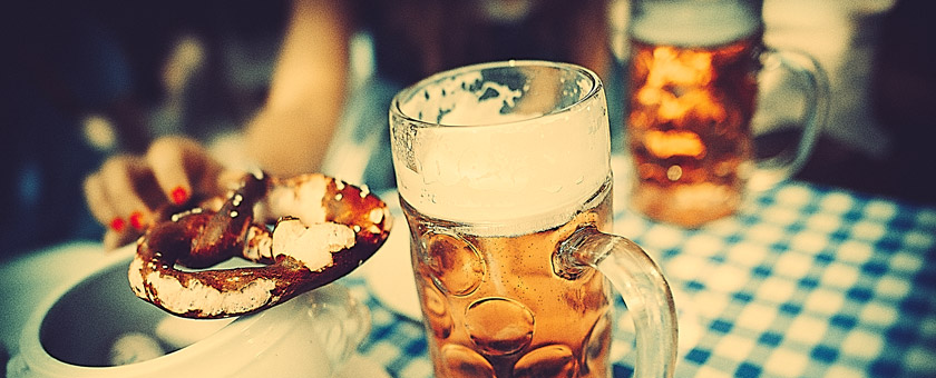 Auf einem Bierzelt-Tisch stehen zwei Krüge mit Bier. Daneben liegt Laugengebäck.